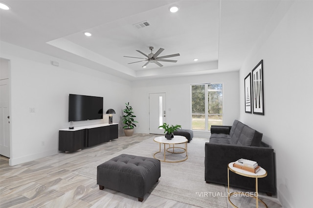 living room with light wood-type flooring, a raised ceiling, and ceiling fan