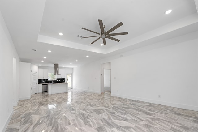 unfurnished living room with a raised ceiling, ceiling fan, and sink