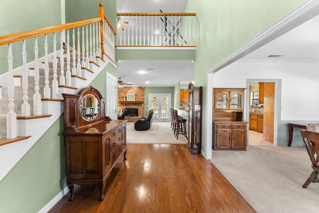 carpeted foyer featuring stairway, wood finished floors, a high ceiling, crown molding, and a brick fireplace