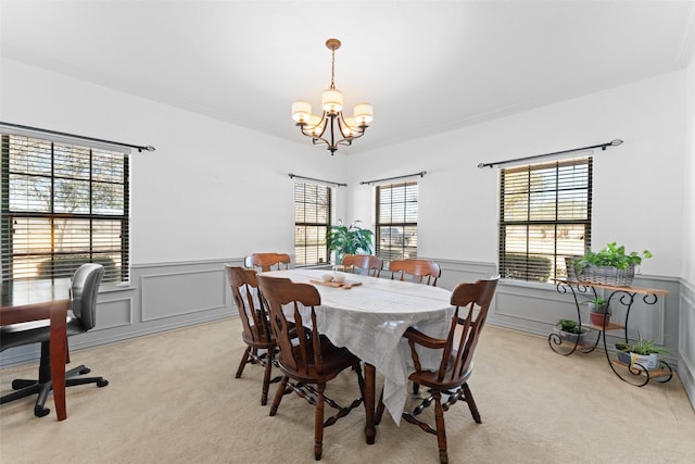 dining area with an inviting chandelier, light colored carpet, and wainscoting