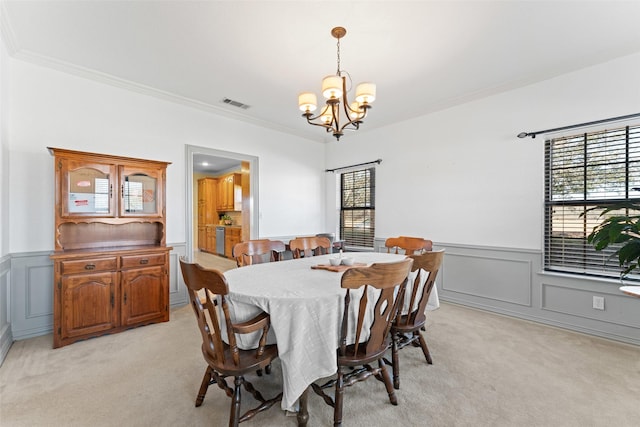 dining room featuring a notable chandelier, light colored carpet, ornamental molding, and a wainscoted wall