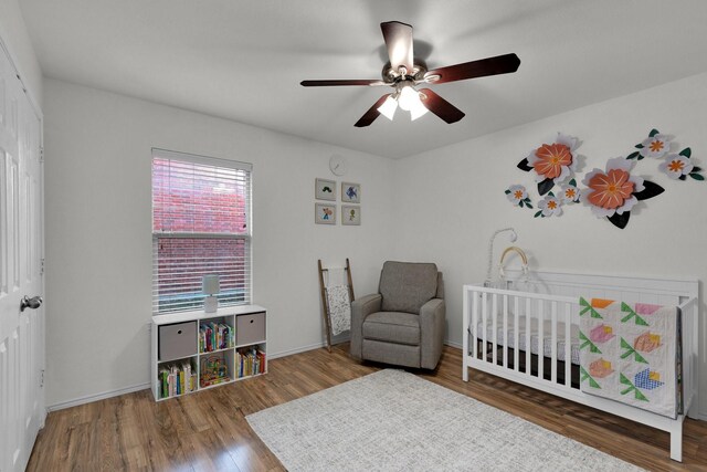 bedroom with a crib, hardwood / wood-style flooring, and ceiling fan