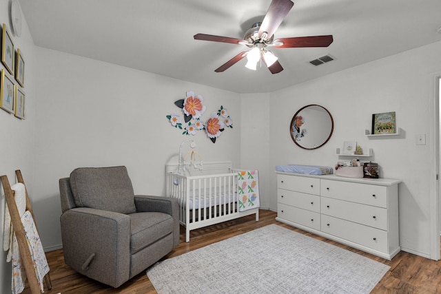 bedroom featuring ceiling fan, dark hardwood / wood-style flooring, and a crib