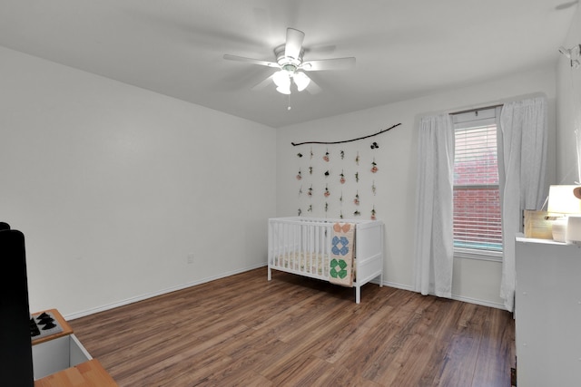 bedroom featuring a crib, ceiling fan, and dark hardwood / wood-style floors