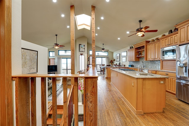 kitchen with light stone countertops, light wood-type flooring, stainless steel appliances, vaulted ceiling, and a center island with sink