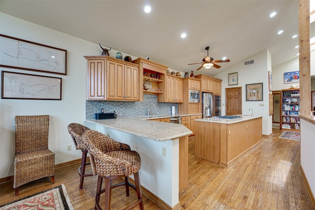 kitchen featuring a center island, vaulted ceiling, light wood-type flooring, kitchen peninsula, and stainless steel appliances