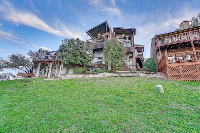 rear view of property featuring a lawn, a balcony, and a wooden deck