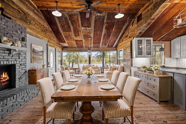 dining area with a stone fireplace, a wealth of natural light, light hardwood / wood-style flooring, and vaulted ceiling