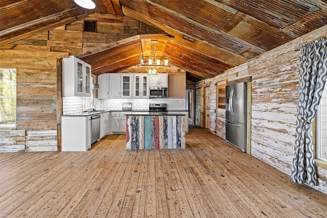 kitchen with light wood-type flooring, stainless steel appliances, white cabinetry, and wood walls