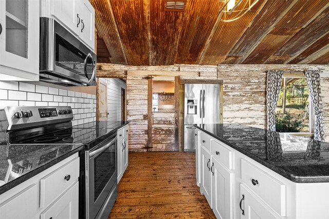 kitchen with white cabinetry, dark wood-type flooring, wood walls, dark stone counters, and appliances with stainless steel finishes