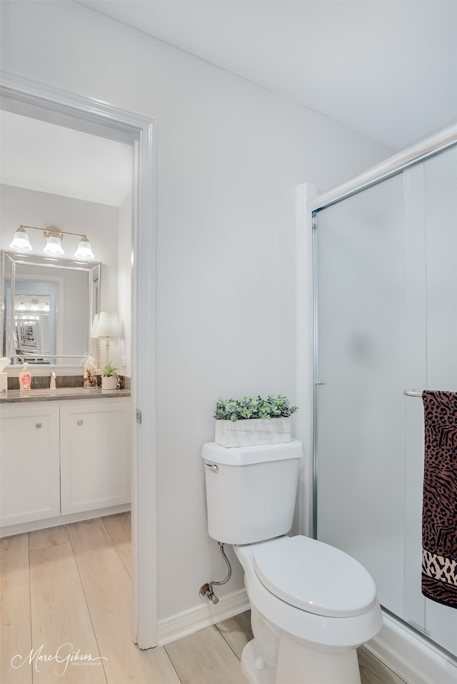 bathroom with wood-type flooring, vanity, toilet, and a shower with shower door