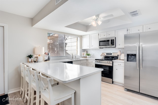 kitchen with white cabinets, a kitchen breakfast bar, light wood-type flooring, kitchen peninsula, and stainless steel appliances