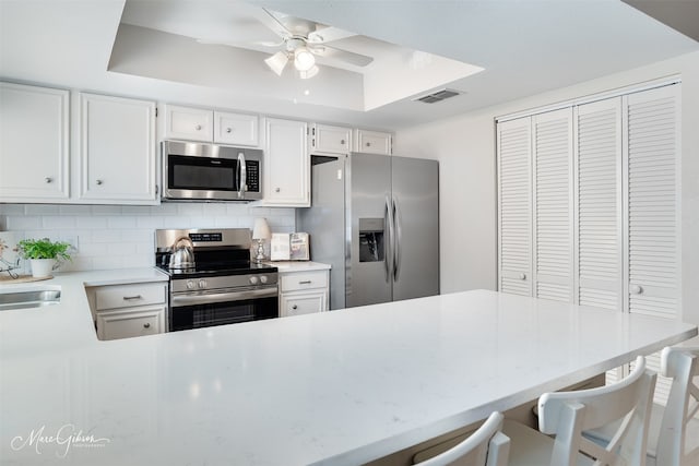 kitchen featuring white cabinetry, a breakfast bar area, appliances with stainless steel finishes, and a tray ceiling