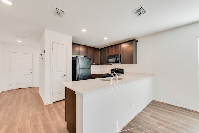 kitchen with kitchen peninsula, light wood-type flooring, dark brown cabinetry, sink, and black appliances