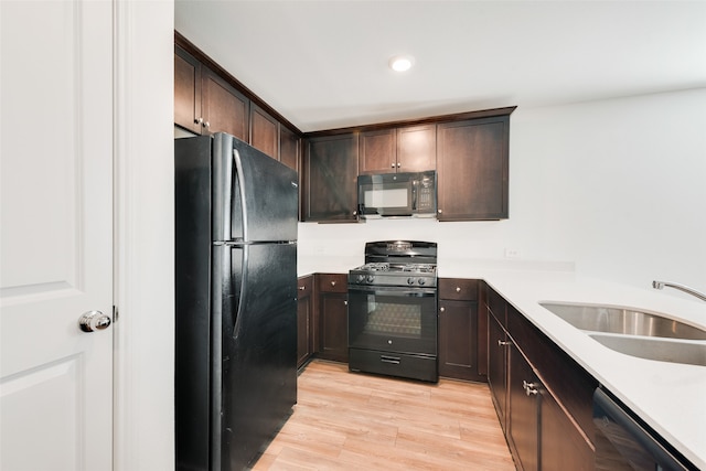 kitchen with black appliances, dark brown cabinetry, sink, and light hardwood / wood-style flooring