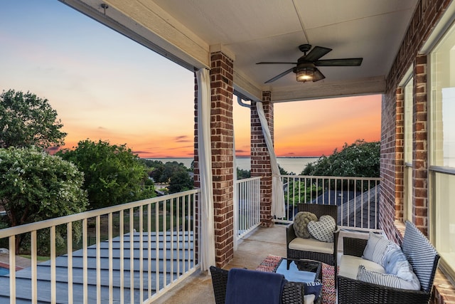 balcony at dusk with a water view and ceiling fan