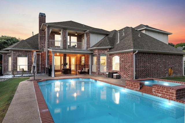 back house at dusk featuring a pool with hot tub, ceiling fan, a balcony, and a patio