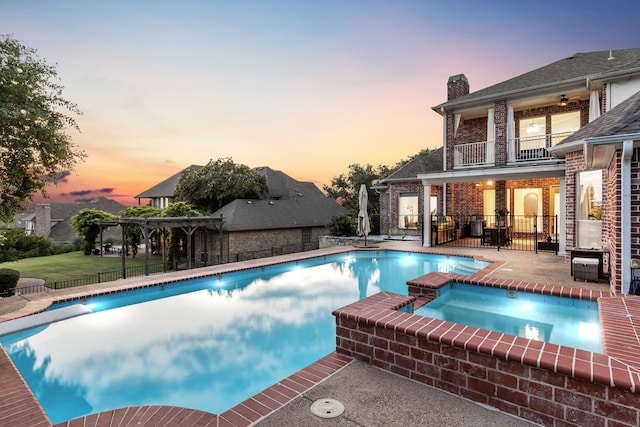 pool at dusk with an in ground hot tub and a patio