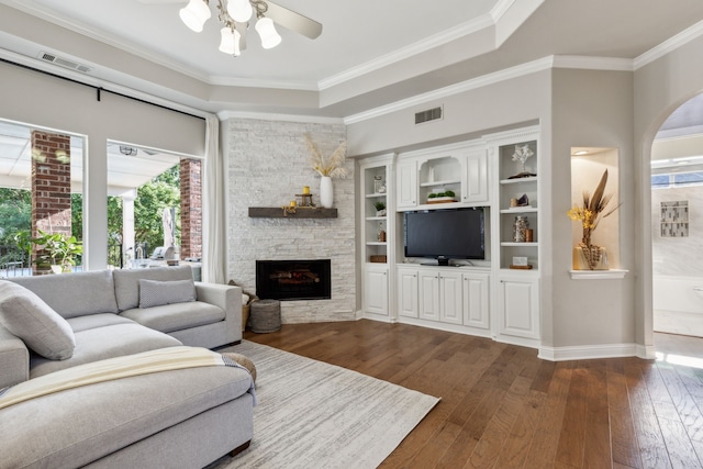 living room with ornamental molding, dark wood-type flooring, a stone fireplace, and a healthy amount of sunlight