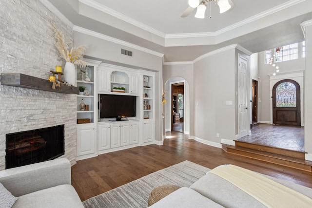 living room featuring dark hardwood / wood-style flooring, a stone fireplace, ceiling fan, and ornamental molding