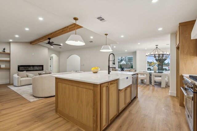 kitchen with a kitchen island with sink, sink, decorative light fixtures, light hardwood / wood-style floors, and stainless steel appliances