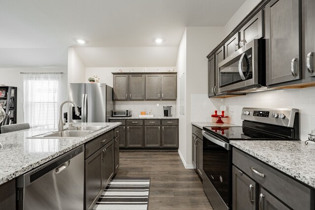 kitchen featuring light stone countertops, appliances with stainless steel finishes, dark hardwood / wood-style flooring, backsplash, and sink