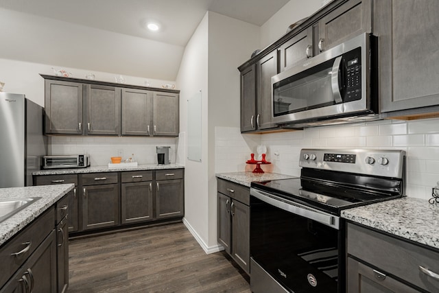 kitchen featuring tasteful backsplash, light stone counters, dark hardwood / wood-style flooring, and appliances with stainless steel finishes