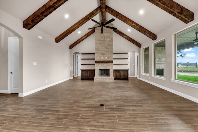 unfurnished living room featuring beam ceiling, high vaulted ceiling, a stone fireplace, and ceiling fan