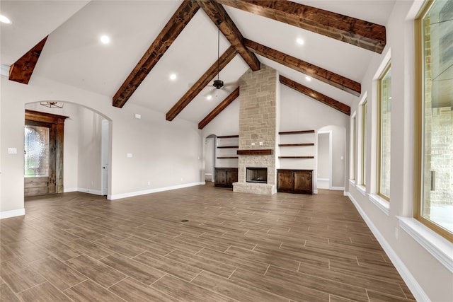 unfurnished living room featuring beam ceiling, a stone fireplace, high vaulted ceiling, and wood-type flooring