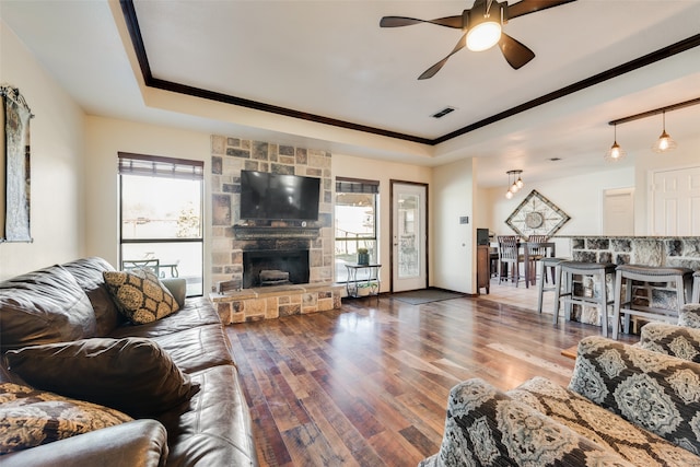 living room featuring a raised ceiling, ceiling fan, a fireplace, and wood-type flooring