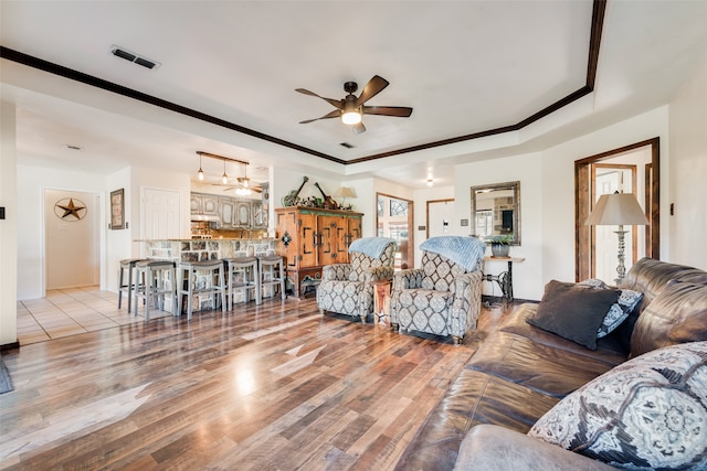 living room with a tray ceiling, ceiling fan, light hardwood / wood-style flooring, and ornamental molding