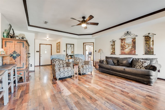 living room featuring a raised ceiling, ceiling fan, light hardwood / wood-style floors, and ornamental molding