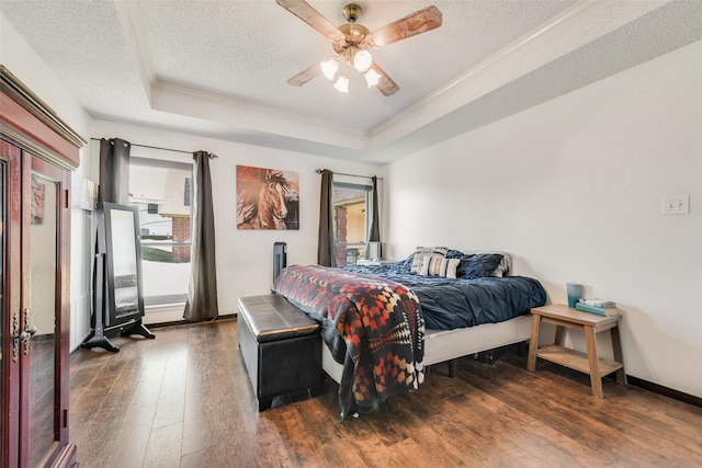 bedroom with ceiling fan, dark hardwood / wood-style floors, a textured ceiling, a tray ceiling, and ornamental molding