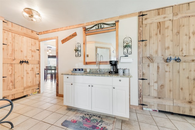 kitchen featuring wood walls, white cabinets, sink, light tile patterned flooring, and light stone counters