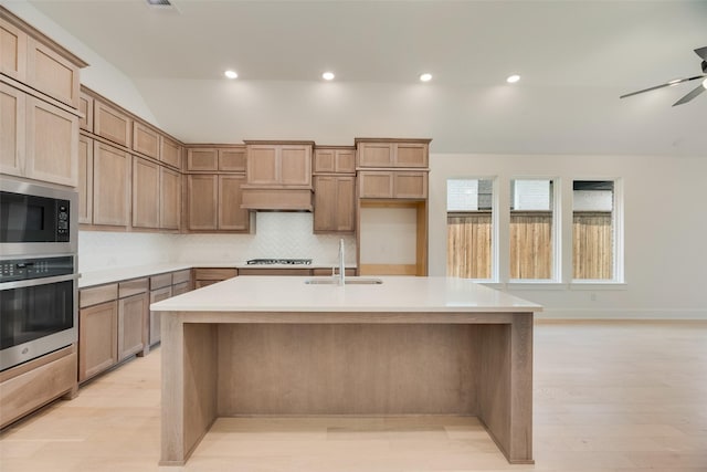 kitchen featuring decorative backsplash, a kitchen island with sink, built in microwave, a sink, and stainless steel oven