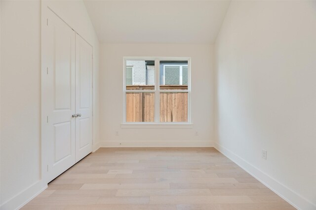 unfurnished bedroom with light wood-style floors, baseboards, and vaulted ceiling