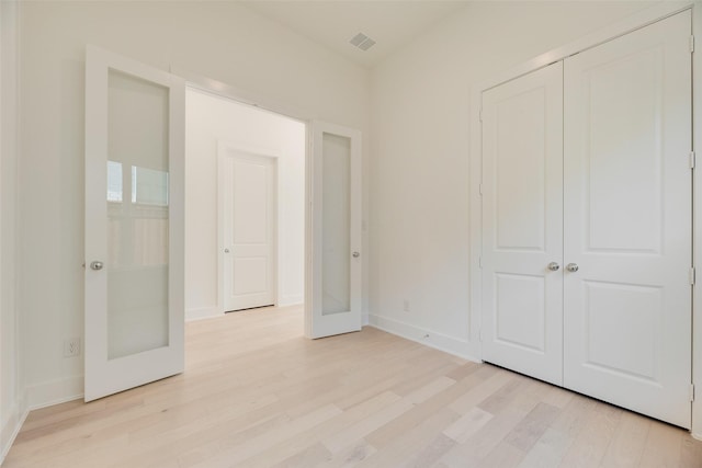 unfurnished bedroom featuring french doors, visible vents, light wood-type flooring, baseboards, and a closet