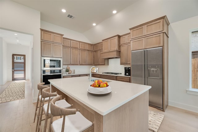 kitchen with a sink, light wood-style flooring, stainless steel appliances, backsplash, and visible vents