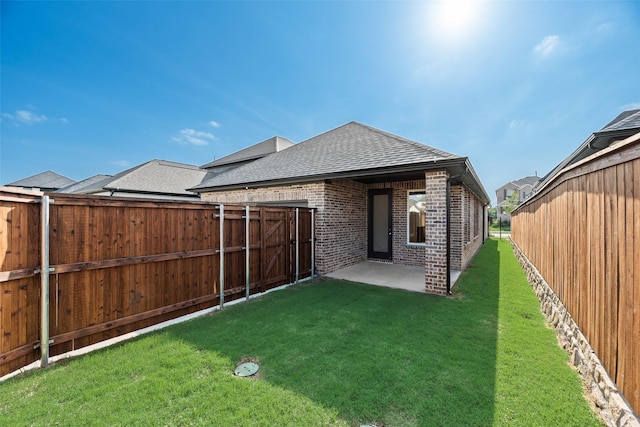 back of property featuring roof with shingles, brick siding, a fenced backyard, a patio, and a yard