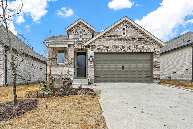 french country style house with a garage, entry steps, concrete driveway, roof with shingles, and brick siding