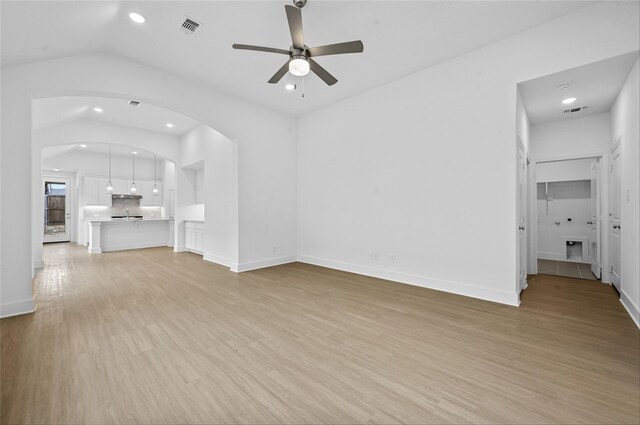 kitchen with a kitchen island with sink, hanging light fixtures, light wood-type flooring, white cabinetry, and stainless steel appliances