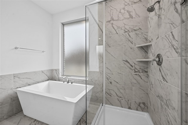 full bathroom featuring a stall shower, a wainscoted wall, marble finish floor, a freestanding tub, and tile walls