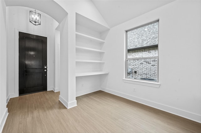 entryway featuring arched walkways, an inviting chandelier, vaulted ceiling, wood finished floors, and baseboards