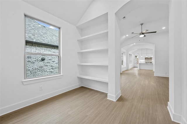 spare room with built in shelves, arched walkways, vaulted ceiling, and wood finished floors