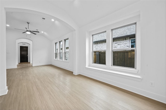 unfurnished living room featuring arched walkways, lofted ceiling, light wood-style floors, a ceiling fan, and baseboards