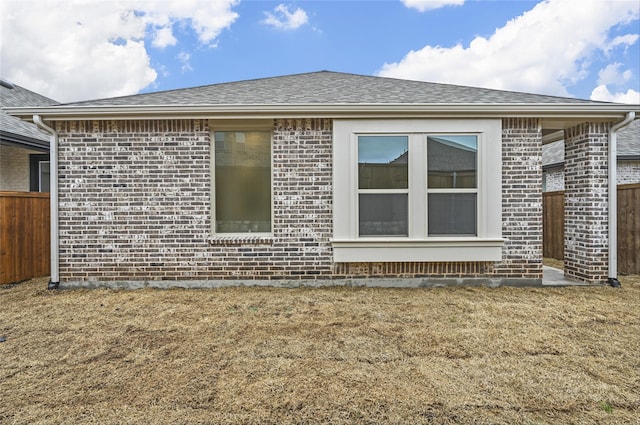 view of home's exterior featuring brick siding, roof with shingles, and fence