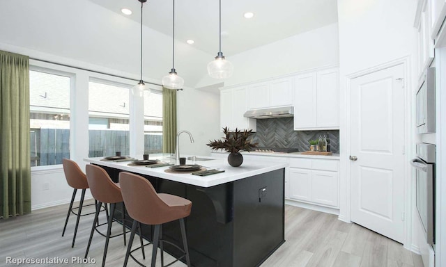 kitchen featuring light hardwood / wood-style flooring, pendant lighting, decorative backsplash, a center island with sink, and white cabinets