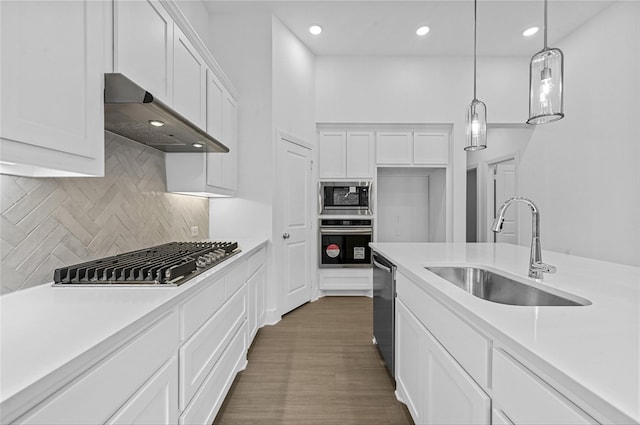 kitchen with stainless steel appliances, light countertops, under cabinet range hood, white cabinetry, and a sink