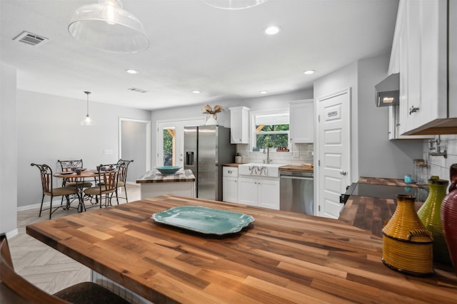 kitchen featuring butcher block counters, white cabinetry, hanging light fixtures, stainless steel appliances, and decorative backsplash