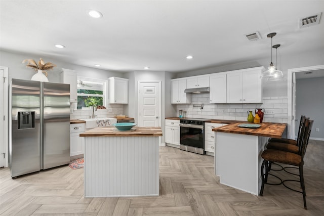 kitchen with stainless steel appliances, white cabinetry, a kitchen island, and wooden counters